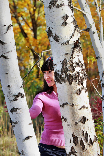 Beautiful girl looks out from behind a birch - Zdjęcie, obraz