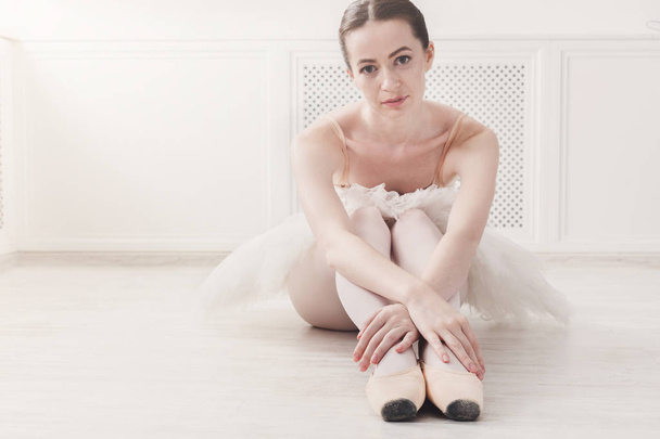 Closeup of young ballerina sit in pointe shoes on white floor background - Photo, Image