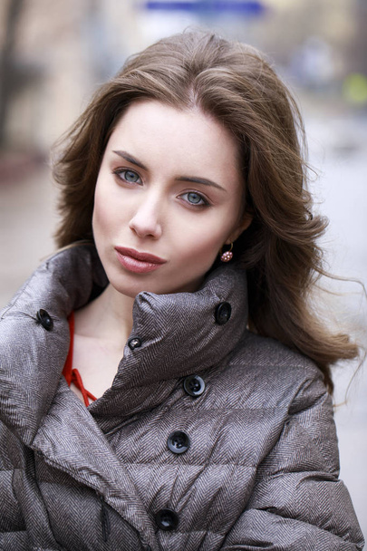 Portrait of a Young stylish brunette girl in a gray down jacket  - Фото, изображение