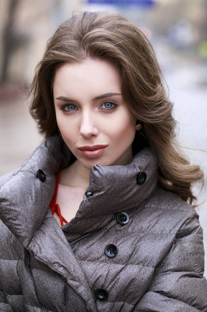 Portrait of a Young stylish brunette girl in a gray down jacket  - Фото, изображение