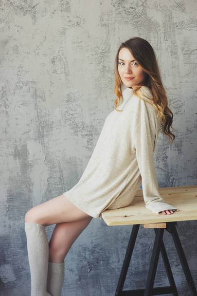 young woman in oversize knitted sweater posing by the grey wall in modern apartment. Casual lifestyle at home - Foto, afbeelding