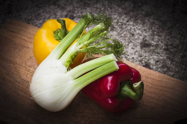 Red and yellow peppers are on a wooden tray with a wonderful fennel - Фото, зображення