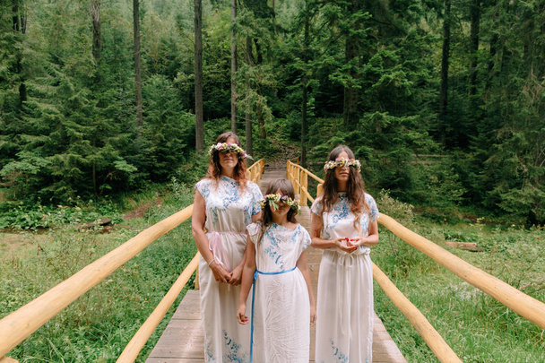 Moeder en twee dochters, wandelen in de buurt van het meer van witte jurkjes met kransen van wilde bloemen - Foto, afbeelding