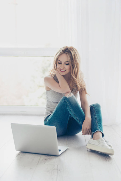 Pretty smiling cute girl sitting on the floor and using laptop - Fotó, kép