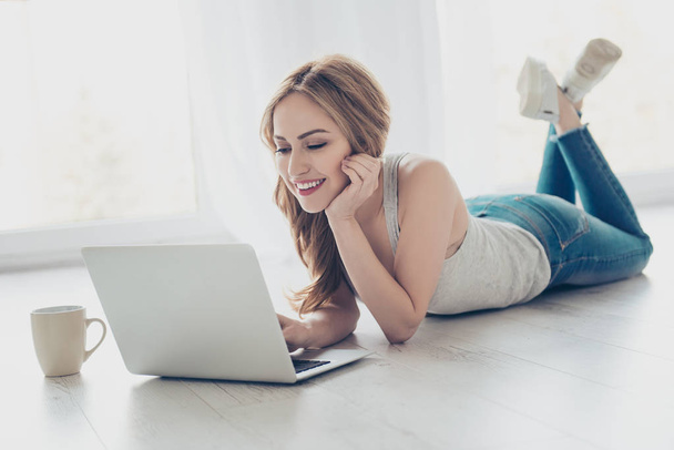 Pretty smiling cute girl lying on the floor and using laptop - 写真・画像