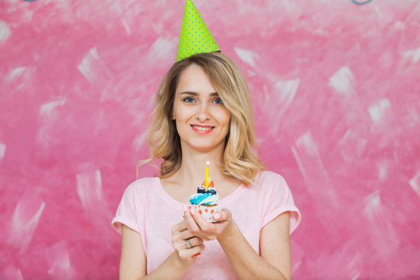 Bonita chica rubia en gorra de cumpleaños sostener cupcake con vela
 - Foto, Imagen
