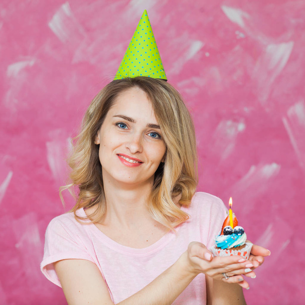 Bonita chica rubia en gorra de cumpleaños sostener cupcake con vela
 - Foto, imagen
