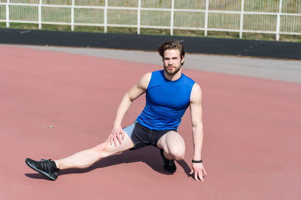 athletic bearded man with muscular body stretching on running track - Фото, изображение