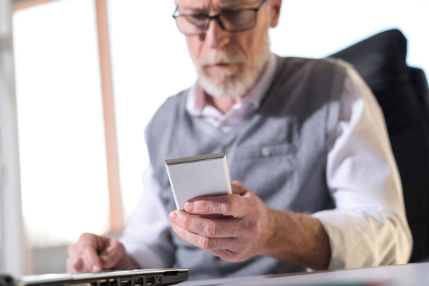 Senior zakenman lezen van een bericht op zijn mobiele telefoon, harde l - Foto, afbeelding