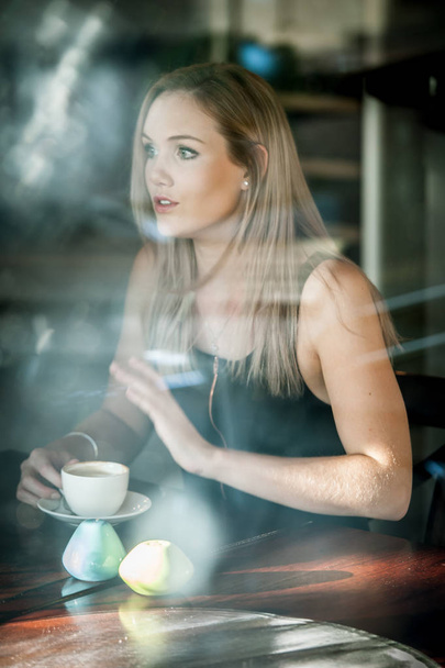 Girl sat in the window of a coffee shop drinking coffee - Foto, afbeelding