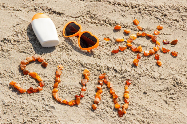 Word and shape of sun, sunglasses with sun lotion on sand at beach, summer time - 写真・画像