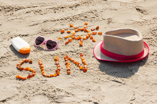 Word and shape of sun, sunglasses, sun lotion and straw hat on sand at beach, summer time - Φωτογραφία, εικόνα
