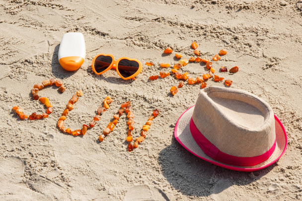 Word and shape of sun, sunglasses, sun lotion and straw hat on sand at beach, summer time - Photo, image