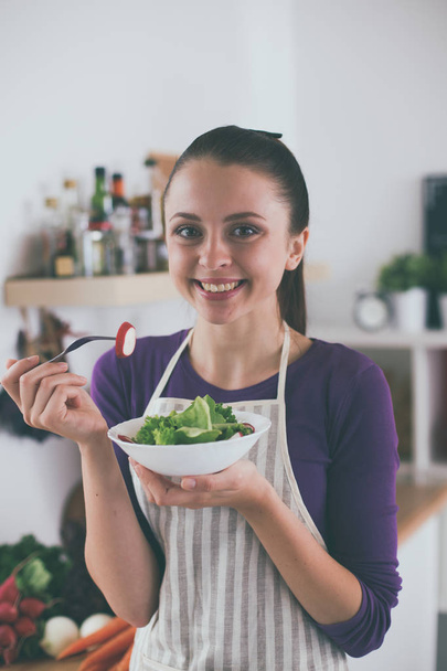 Young woman eating fresh salad in modern kitchen - Foto, afbeelding