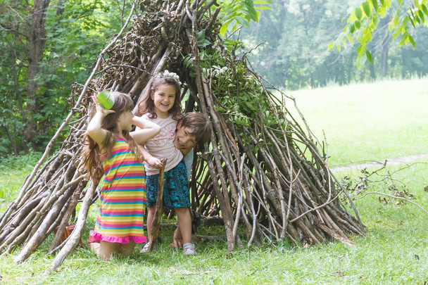 木の棒の家の隣に遊ぶ子供たち - 写真・画像