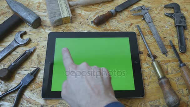 Αρσενική χέρι του μάστορα τεχνίτη χρησιμοποιώντας pc ταμπλετών με πράσινη οθόνη στο εργαστήριο. Το Top view. Διαφορετικά εκλεκτής ποιότητας εργαλεία βρίσκονται δίπλα - Πλάνα, βίντεο