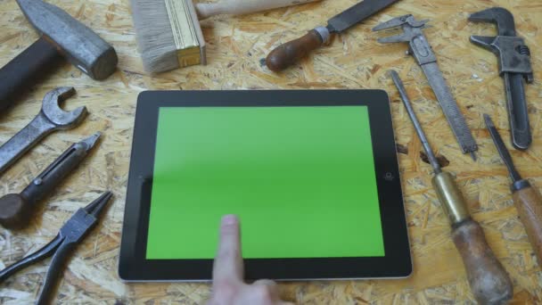 Mano masculina de artesano usando tableta pc con pantalla verde en el taller. Vista superior. Diferentes herramientas vintage se encuentran al lado
 - Imágenes, Vídeo