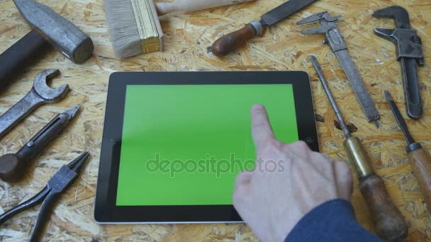 Εκμετάλλευση tablet pc σε λειτουργία τοπίο με εργαστήριο τραπέζι με Ξυλουργικά εργαλεία στο παρασκήνιο. Ο άνθρωπος χέρι χρησιμοποιώντας tablet με πράσινη οθόνη. Το Top View - Πλάνα, βίντεο