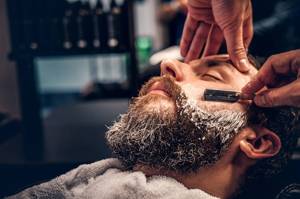 Peluquero afeitando a un hombre con una navaja afilada
 - Foto, imagen
