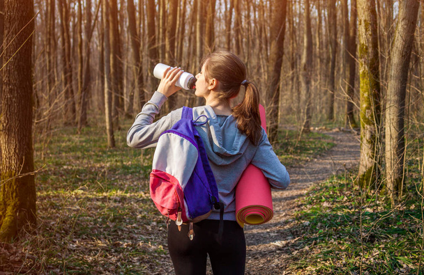 Kız uzun yürüyüşe çıkan kimse sırt çantası ile ormanda suyu içer - Fotoğraf, Görsel