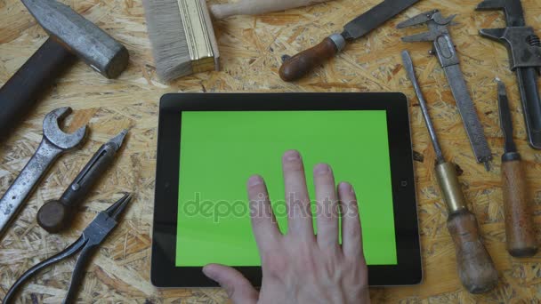 Male hand of artisan craftsman using tablet pc with green screen in workshop. Top view. Different vintage tools lie beside - Footage, Video