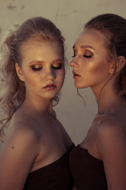 Glamour-Make-up zwei Frauen mit langen Frisuren, die im Dunkeln auf der Straßenmauer sitzen. Modefarbenporträt - Foto, Bild