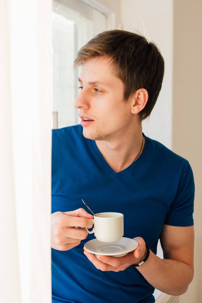 Ο άνθρωπος που πίνει καφέ κοιτάζοντας έξω από το παράθυρο - Φωτογραφία, εικόνα