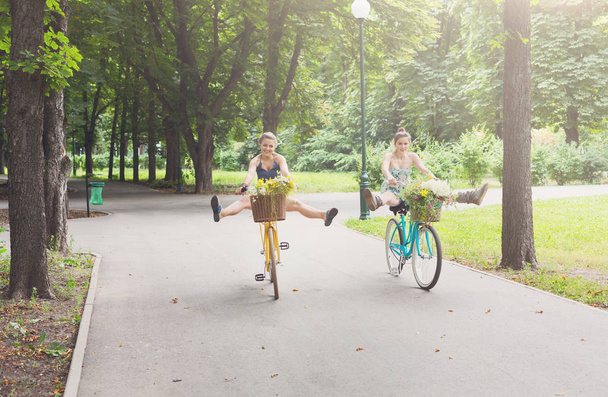 Felice boho chic ragazze cavalcare insieme su biciclette nel parco
 - Foto, immagini
