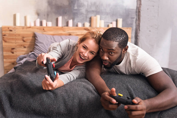 Merry international couple playing video games at home - Foto, Imagen