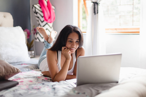 Chica adolescente en el dormitorio mirando a la computadora portátil
 - Foto, imagen