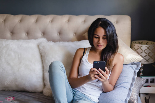 Teenage girl in bedroom using smartphone - 写真・画像
