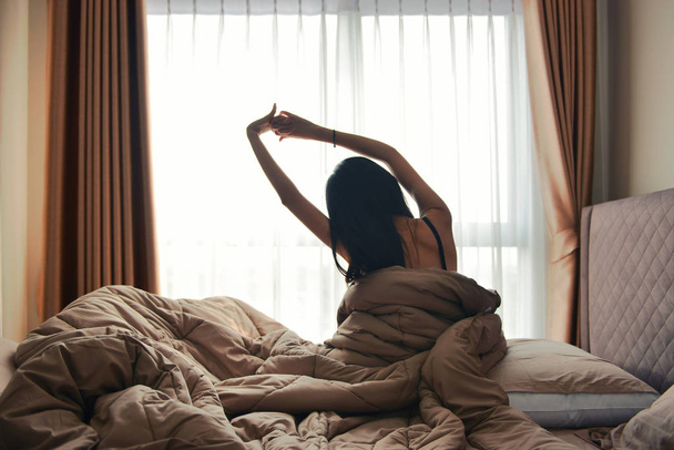 Счастливая женщина с видом сзади, просыпаясь в постельном номере отеля
 - Фото, изображение