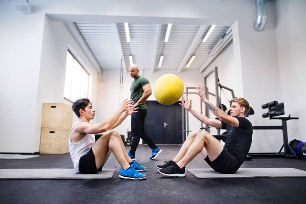 Men in gym with trainer exercising with medicine balls. - Photo, image