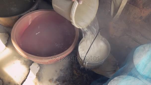 Gros plan sur un homme ramollissant la pâte de riz avec de l'eau dans un seau troué
 - Séquence, vidéo