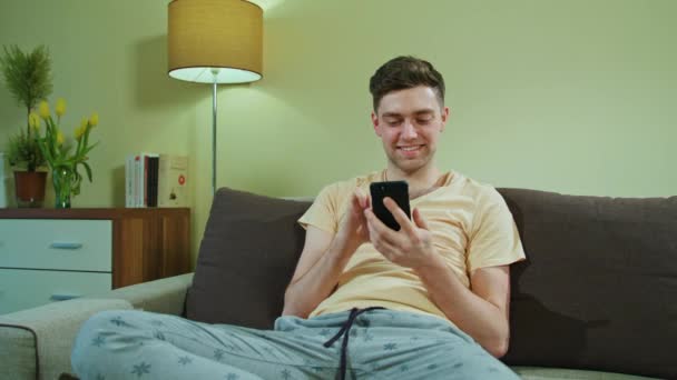 Man Sitting on the Sofa and Using Mobile Phone - Filmati, video