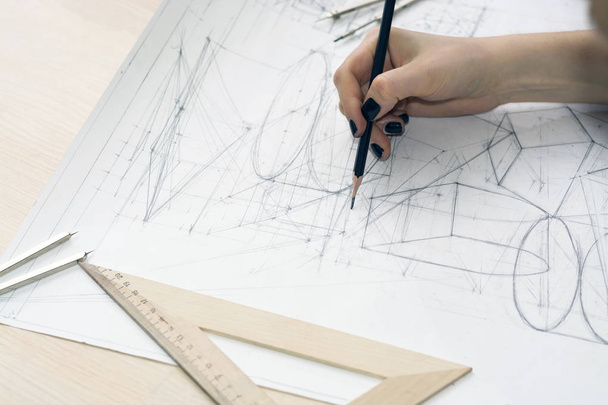 Κορίτσι αρχιτέκτονα σύρει ένα σχέδιο, σχέδιο, γεωμετρικά σχήματα από μολύβι σε μεγάλο φύλλο χαρτιού στο γραφείο. - Φωτογραφία, εικόνα