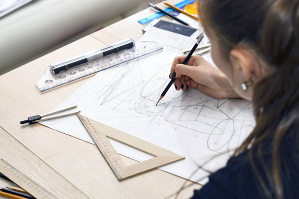Κορίτσι αρχιτέκτονα σύρει ένα σχέδιο, σχέδιο, γεωμετρικά σχήματα από μολύβι σε μεγάλο φύλλο χαρτιού στο γραφείο. - Φωτογραφία, εικόνα
