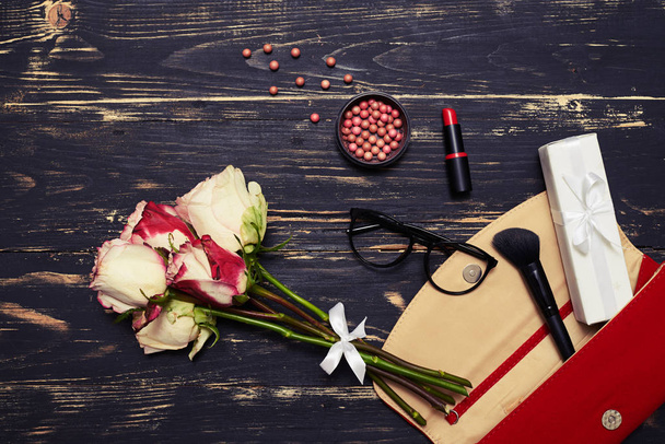 Red bag with cosmetics, glasses and roses on grunge background  - Photo, Image