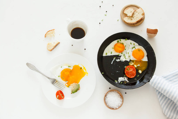 Τρώγοντας στη διαδικασία, τηγανητά αυγά, σε ένα τηγάνι και σε ένα πιάτο, τοστ με αβοκάντο και ένα φλιτζάνι καφέ για πρωινό. - Φωτογραφία, εικόνα