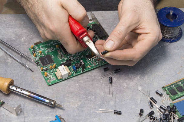 Um trabalhador de serviço eletrônico corta a ponta do capacitor com um alicate
. - Foto, Imagem