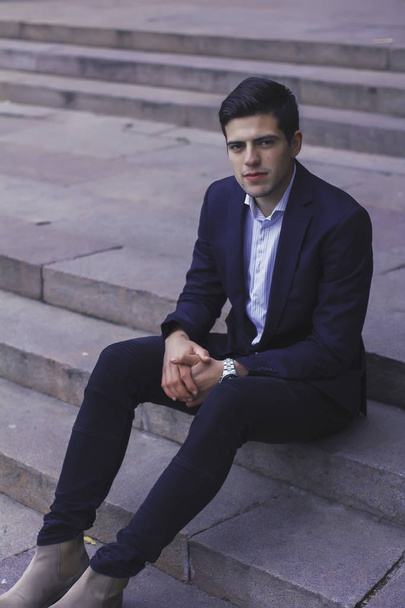 Handsome young man with styled hair. The man is sitting on the steps.  - Foto, Imagen