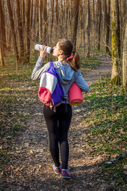 Chica excursionista con mochila bebe agua en el bosque
 - Foto, Imagen