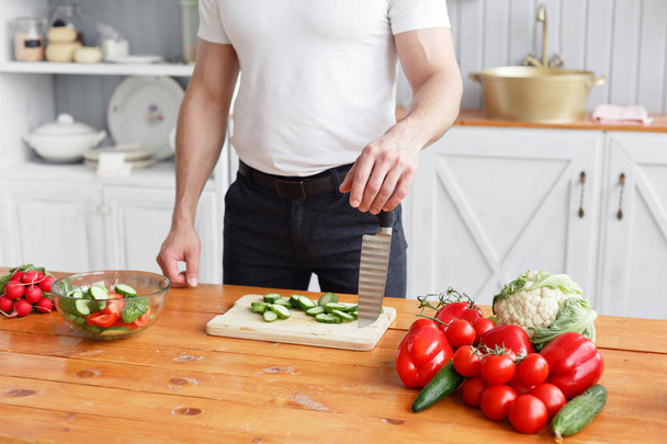 Middle-aged athlete, cuts vegetables salad of cucumber and tomato. Vegetarian food - Fotó, kép