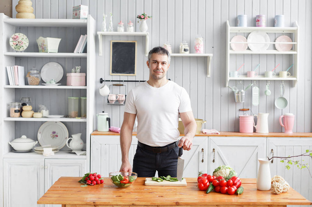 Спортсмен средних лет, режет овощной салат из огурцов и помидоров. Вегетарианская еда
 - Фото, изображение