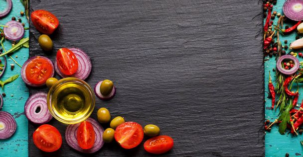 Banner top view on olive oil and ingredients for a healthy salad with cherry tomatoes, onion and olives on natural black slate background with copy space for your text - Photo, Image