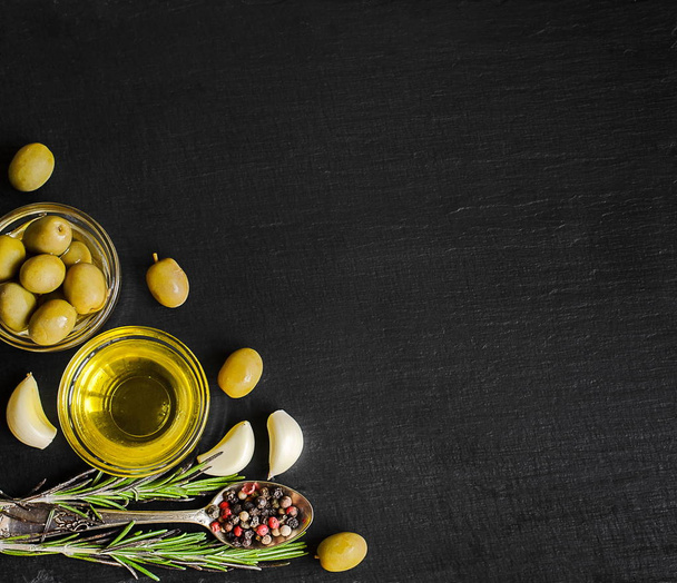 Top view of olive oil and ingredients for a healthy vegetarian salad - cherry tomatoes, olives, garlic and rosemary on natural black slate background with copy space for your text - Photo, Image