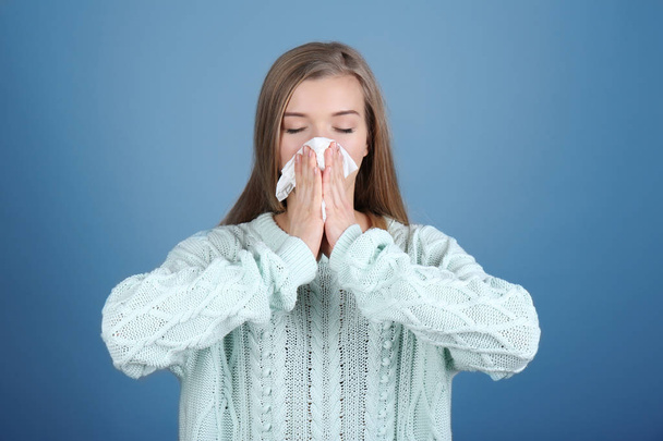 Young woman blowing nose on tissue against color background - Photo, Image