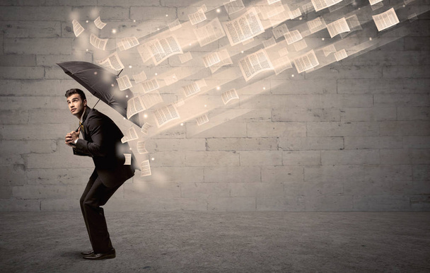 Business man protecting with umbrella against wind of papers - Foto, immagini