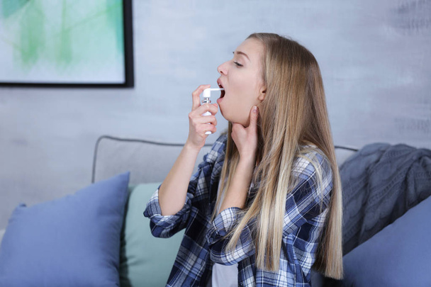 Sick young woman using throat spray at home - Foto, afbeelding