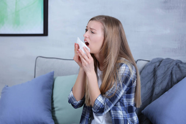 Young woman sneezing into tissue at home - Valokuva, kuva